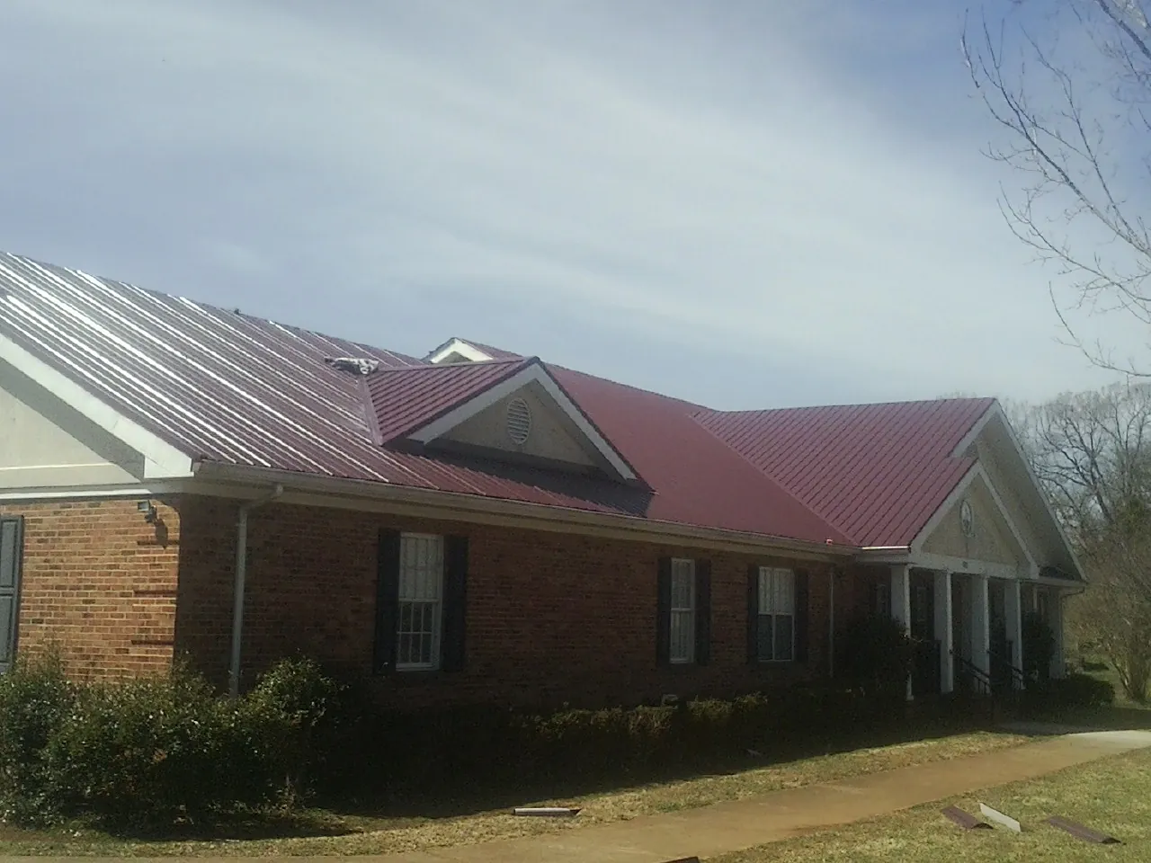 Red metal roof with gabled entries on a long brick building, from a Hail Damage Roof Repair job in Palouse