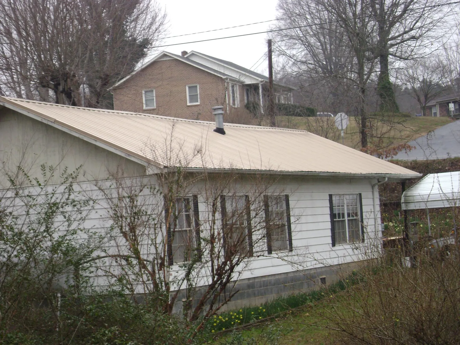 Tan metal roof on a white sided house set into a hillside — Commercial Roofing by Roofing Brothers in Palouse